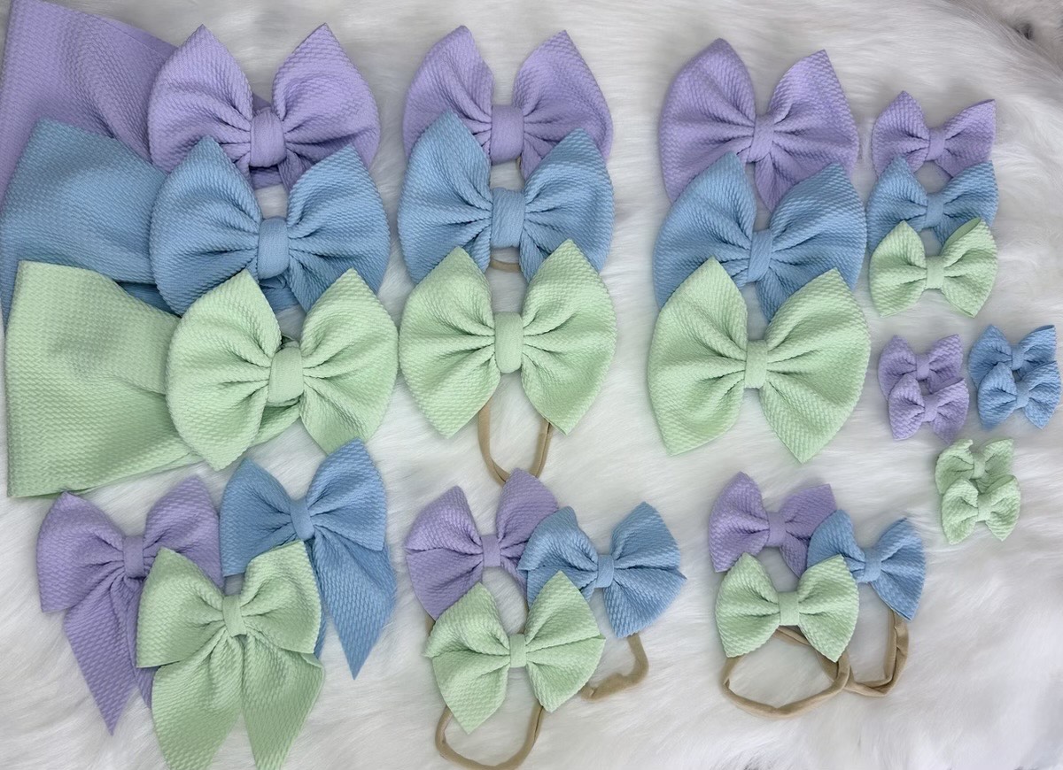 Handmade pastel baby hair bows in lavender, baby blue and mint green — large bows, mini bows and nylon-headband sets arranged on soft white faux fur by Little Addie's Bows